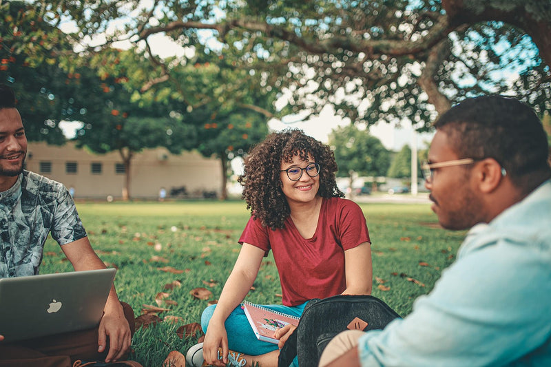 Three people sitting on grass with one using a laptop